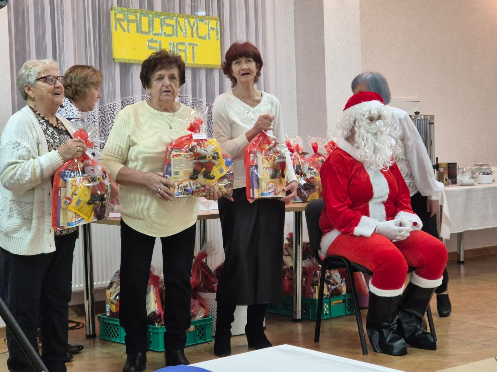 Panie z&nbsp;prezentami świątecznym, na&nbsp;krześle siedzi Mikołaj w&nbsp;stroju