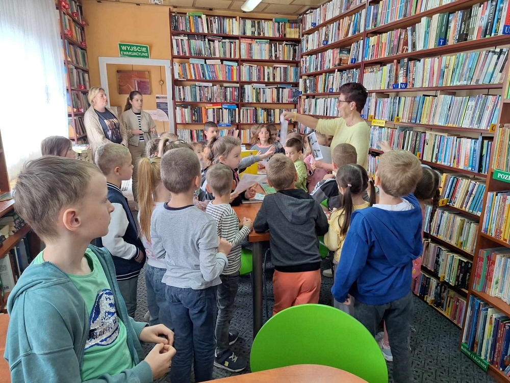Dzieci w bibliotece przeglądają książki na regale
