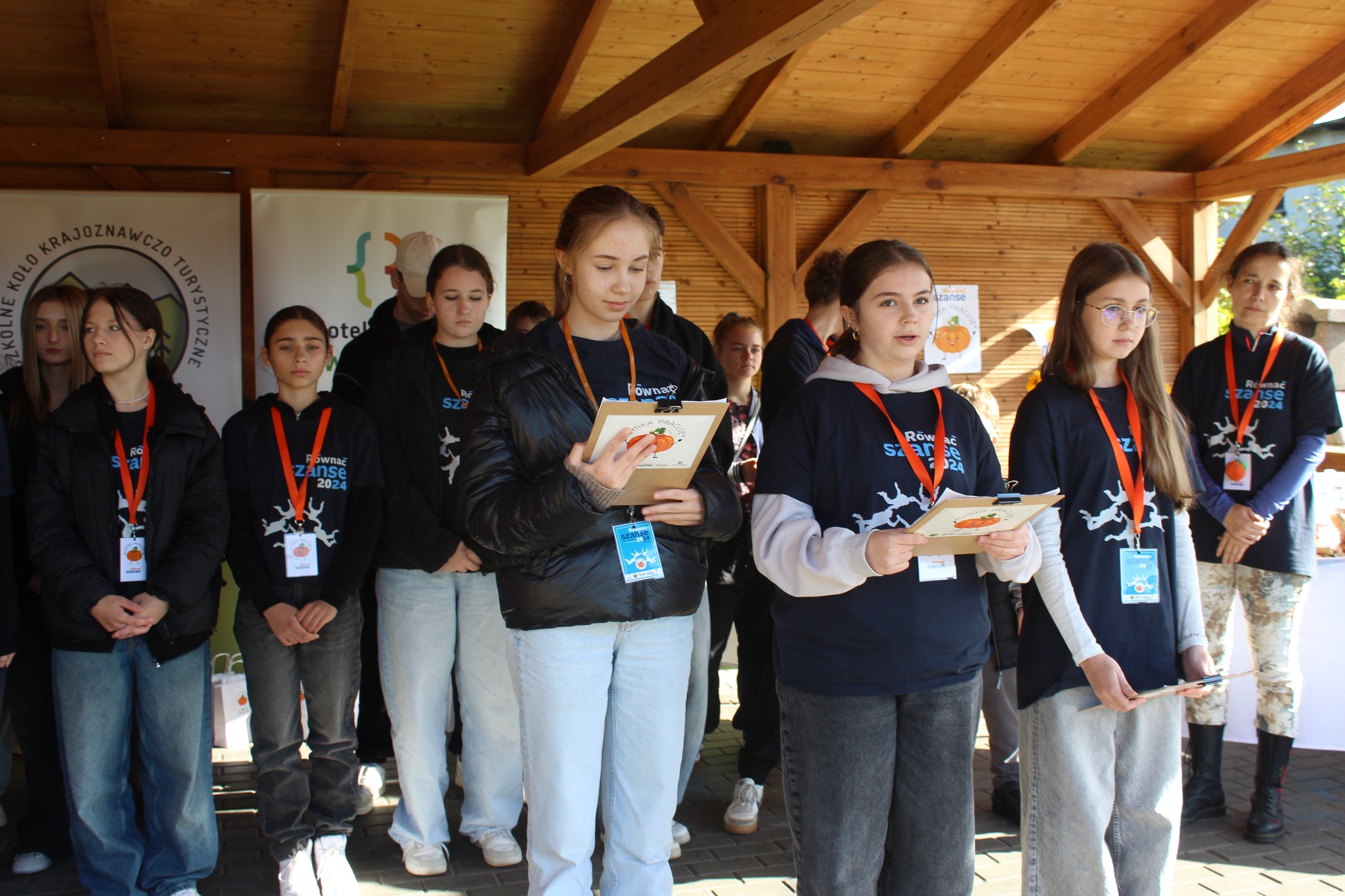 Dziewczyny ubrane w&nbsp;czarne koszulki z&nbsp;napisem r&oacute;wnać szanse, w&nbsp;dłoniach trzymają pomarańczowe teczki