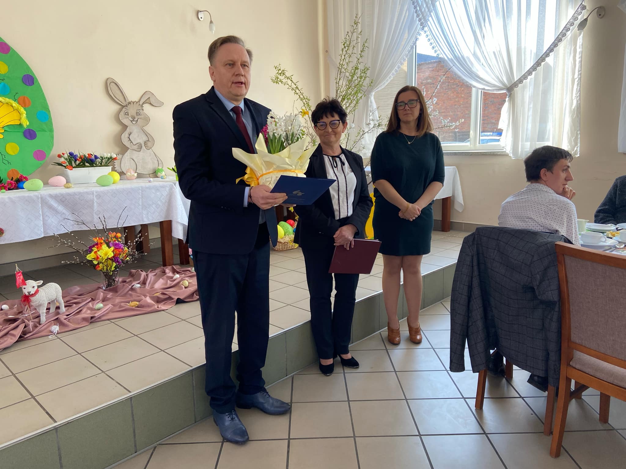 Mężczyzna z koszem kwiatów, obok dwie panie