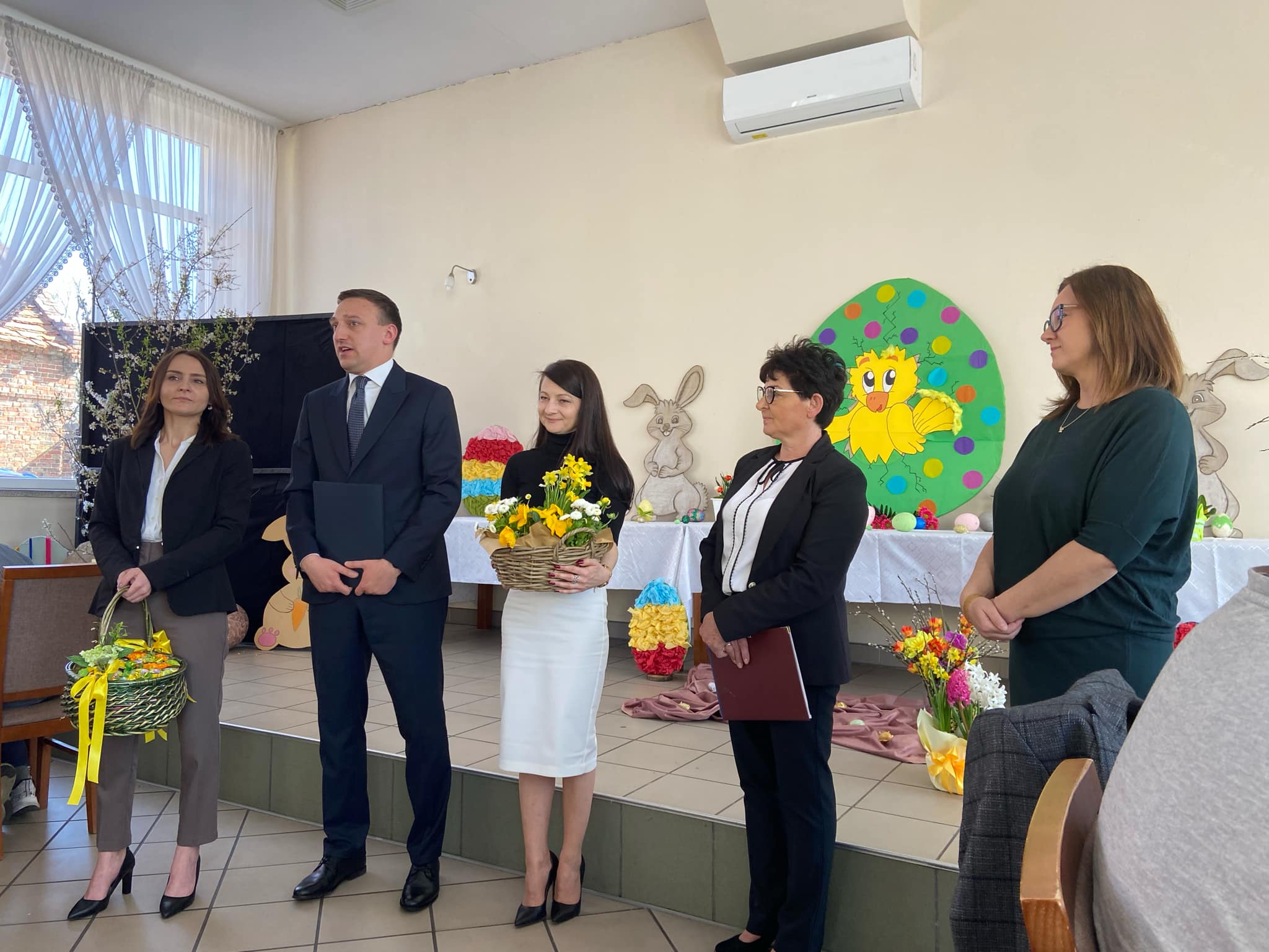 Cztery kobiety z koszami z żółtymi kwiatami, obok mężczyzna w czarnym garniturze