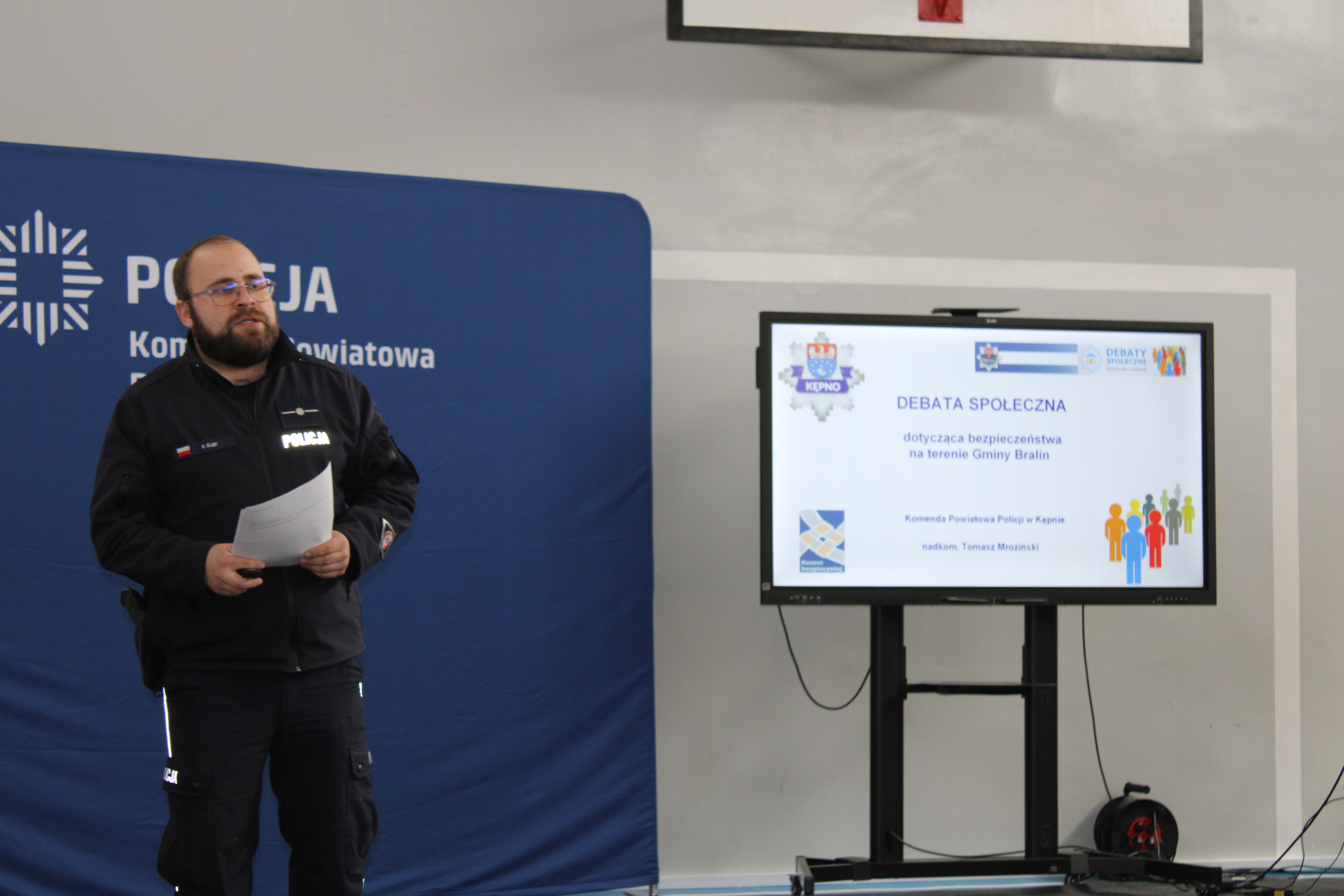 Policjant w&nbsp;mundurze na&nbsp;tle baneru policyjnego