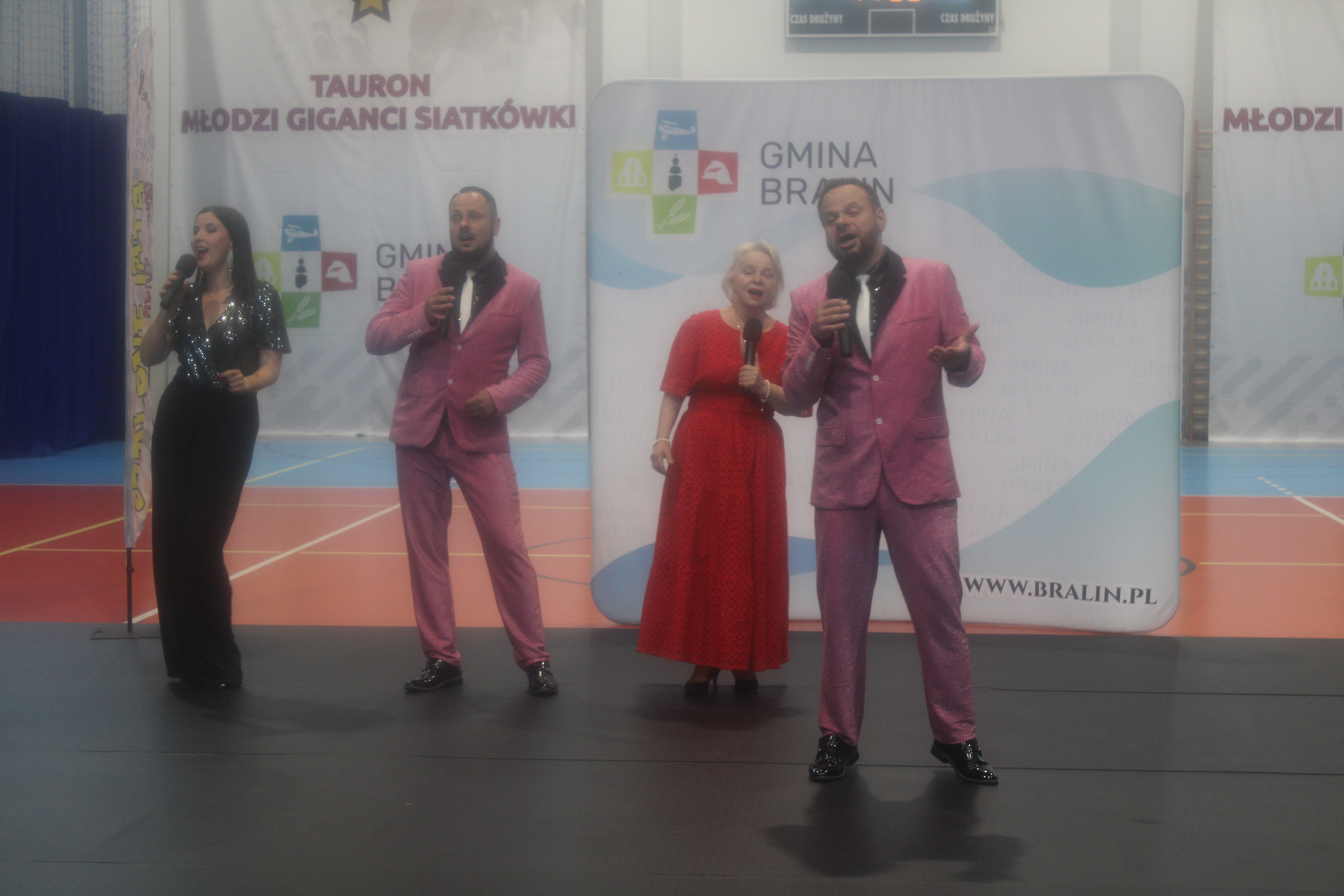 Dwóch mężczyzn w różowych garniturach, dwie panie w sukienkach