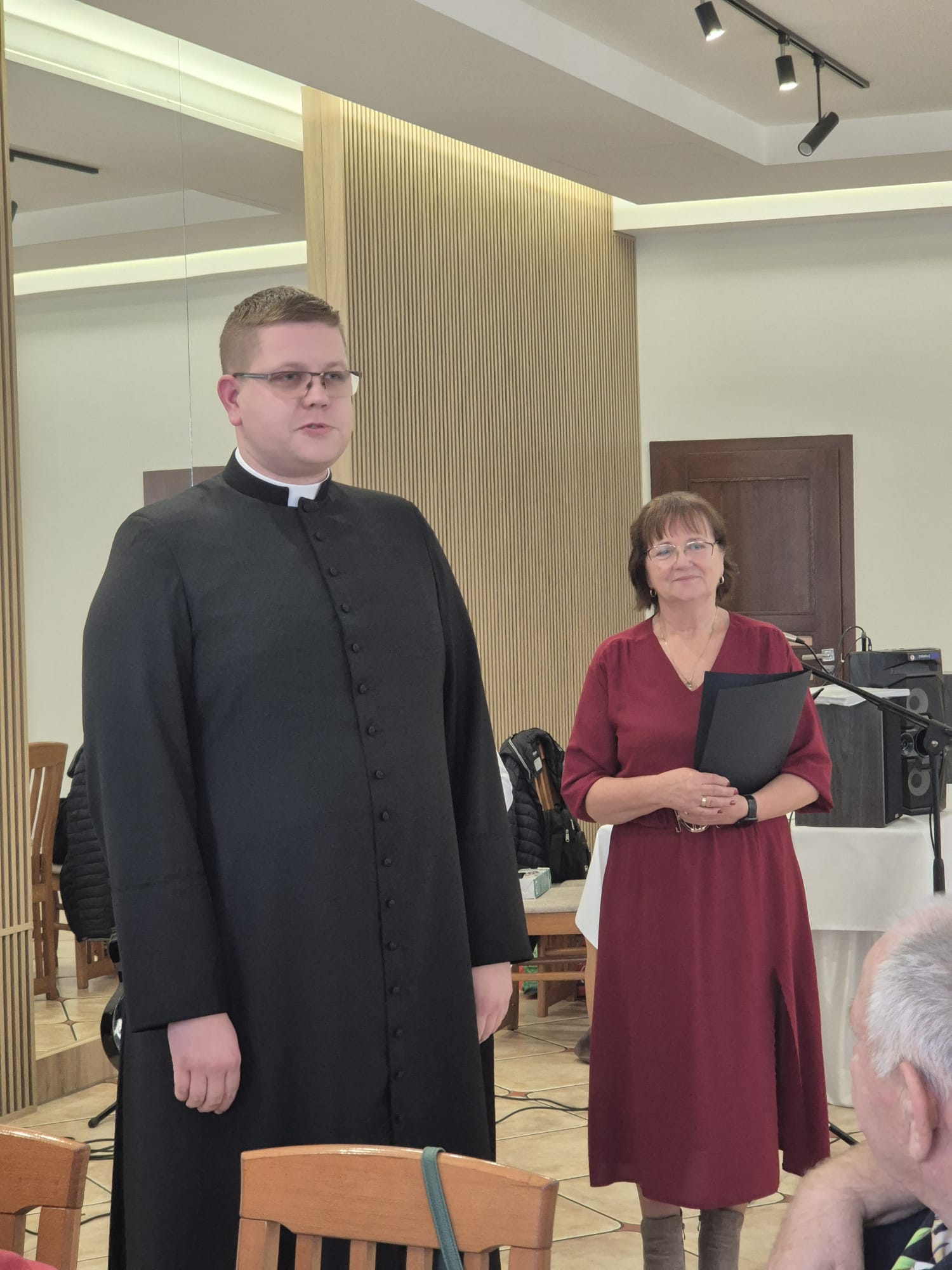 Ksiądz w&nbsp;sułtanie obok pani w&nbsp;bordowej sukience