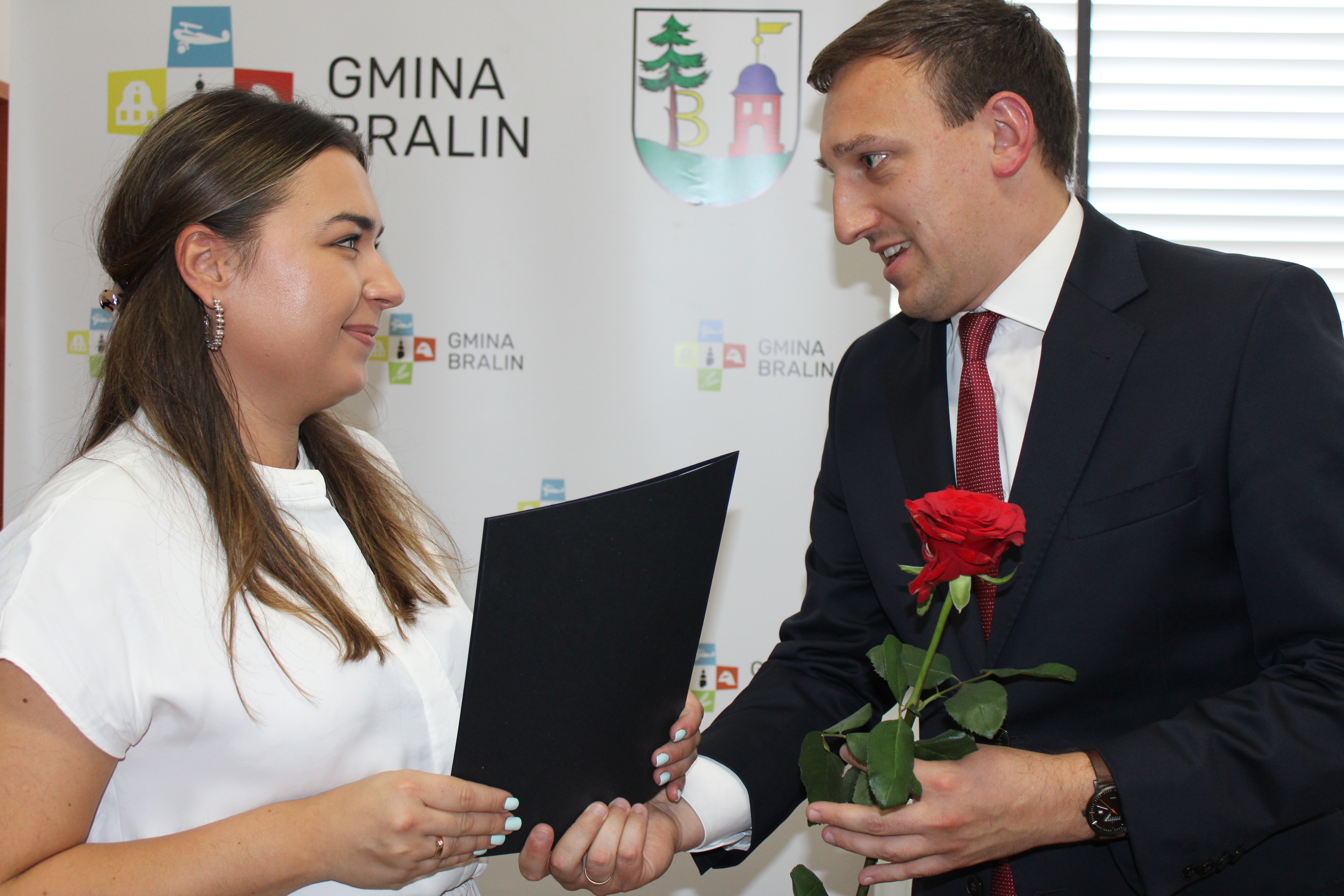 Kobieta w białej bluzce odbiera czerwoną róże od mężczyzny w garniturze