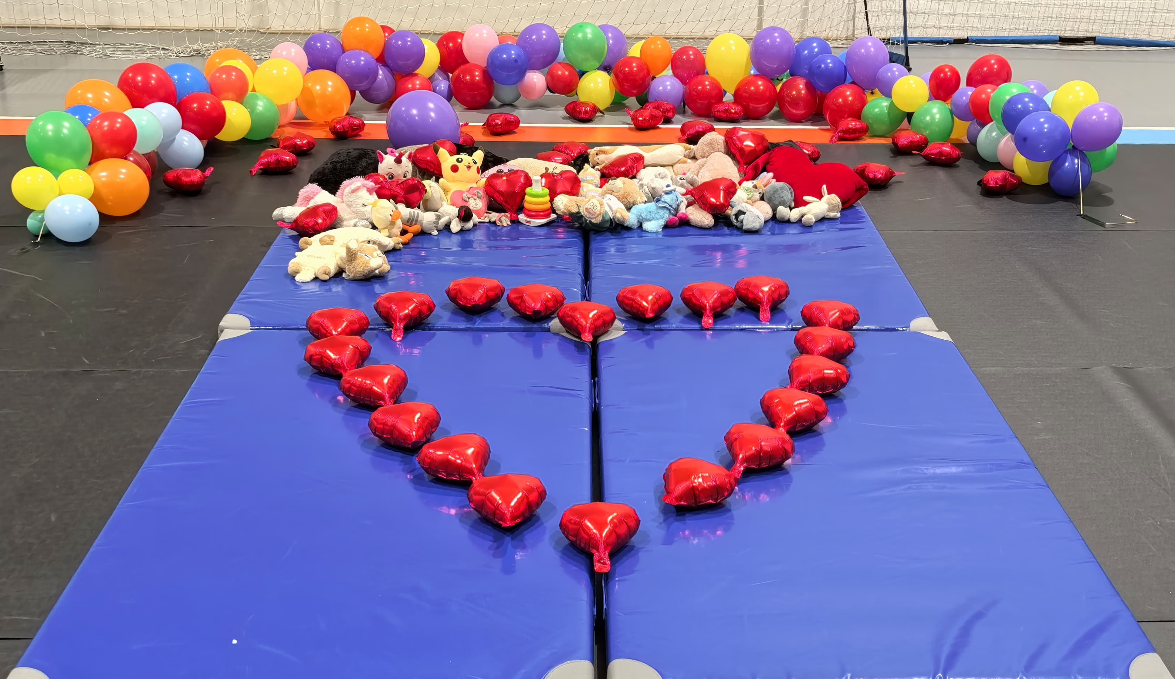 Serduszko z&nbsp;balon&oacute;w na&nbsp;niebieskim materacu, z&nbsp;tyłu maskotki i&nbsp;kolorowe balony