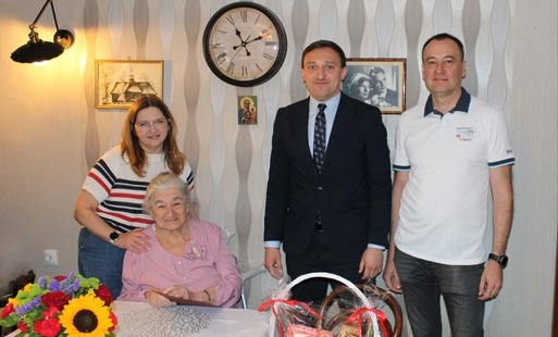 Pani w różowym sweterku, nad nią kobieta obok dwóch meżczyzn, jeden w garniturze drugi w białej koszulce